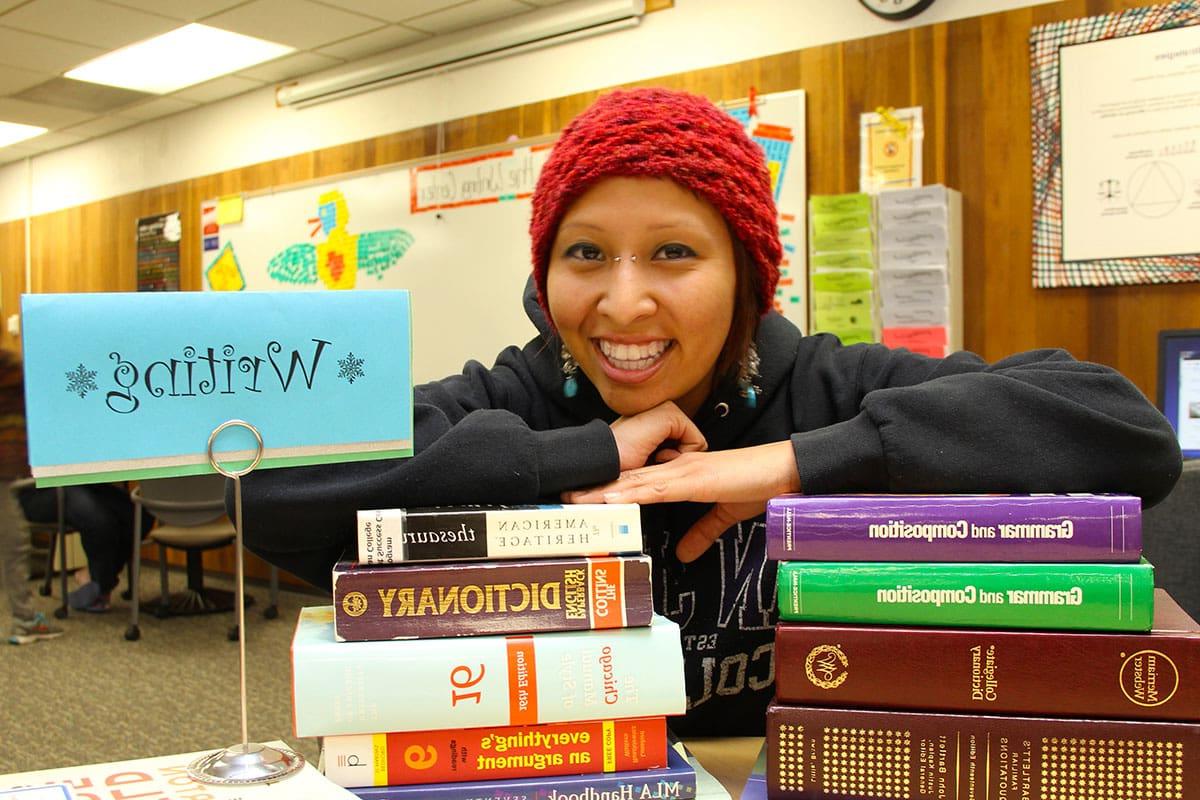 Smiling student in the Tutoring Center with variety of text books.